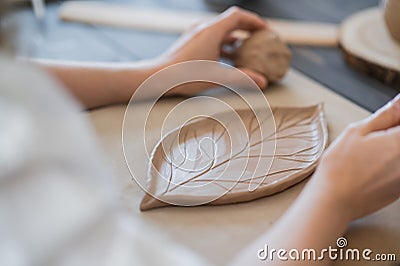 Female hands holding stick and making ornament on decorative product. Clay master moulding clay on a pottery and Stock Photo