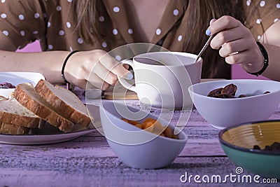 Female hands holding and stirring a cup surrounded by bread on a plate and an assortment of bowls with dry fruits on a wooden Stock Photo