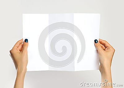 Female hands holding a white booklet triple sheet of paper. Isolated on gray background. Closeup Stock Photo