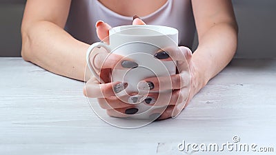 Female hands are holding a white cup of coffee on a light wooden table. The concept of suffering, despair, problems Stock Photo