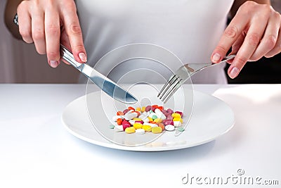 Female hands holds knife and fork and in front of her lie multicolored pills on a white plate. Taking vitamins and supplements. Stock Photo