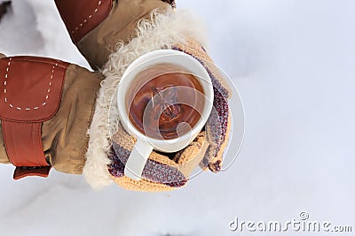 Female hands in knitted grey mittens hold white cup of black spicy tea with anisetree star. Stock Photo