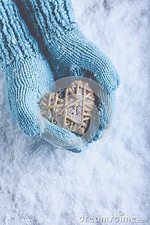 Female hands in light teal knitted mittens with entwined beige flaxen heart on a white snow. Love, St. Valentines Day concept Stock Photo