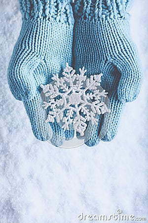 Female hands in light teal knitted mittens with sparkling wonderful snowflake on snow background. Winter and Christmas concept Stock Photo