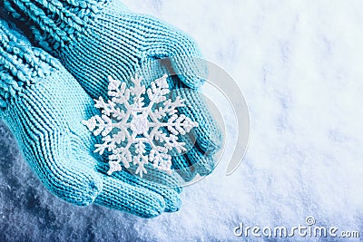 Female hands in light teal knitted mittens with sparkling wonderful snowflake on a white snow background. Winter Christmas concept Stock Photo