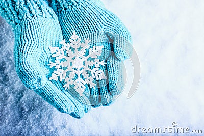 Female hands in light teal knitted mittens with sparkling wonderful snowflake on a white snow background. Winter Christmas concept Stock Photo