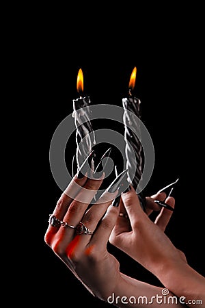 Female hands with long nails hold burning candles on a black background. concept of witchcraft witchcraft on halloween. Stock Photo