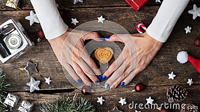 Female hands making a heart shape around a holiday cookie placed in the middle of christmas setting Stock Photo