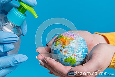 In female hands a model of the globe, which is disinfected with a medical spray, the concept of the global fight against Stock Photo