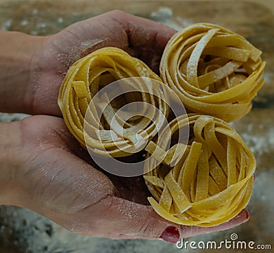 Female hands with pasta on wooden kitchen table powdering by flour Stock Photo