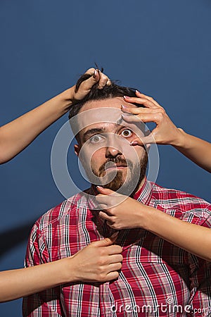 Female hands rumple young bearded handsome man on blue background Stock Photo