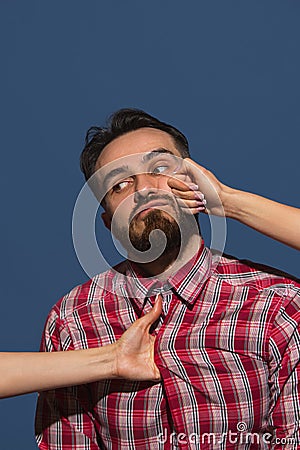 Female hands rumple young bearded handsome man on blue background Stock Photo