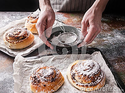 Female hands sprinkle powdered sugar with fresh sweet homemade cinnamon rolls and chocolate cream. Scandinavian cuisine. Hyugge Stock Photo