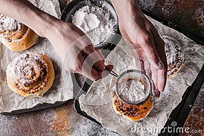 Female hands sprinkle powdered sugar with fresh sweet homemade cinnamon rolls and chocolate cream. Scandinavian cuisine. Hyugge Stock Photo