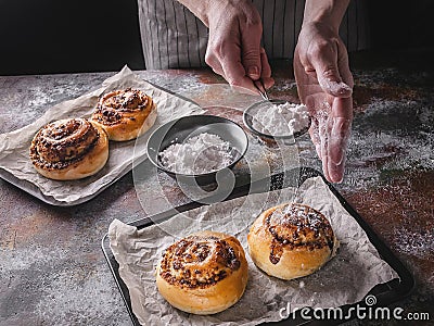 Female hands sprinkle powdered sugar with fresh sweet homemade cinnamon rolls and chocolate cream. Scandinavian cuisine. Hyugge Stock Photo