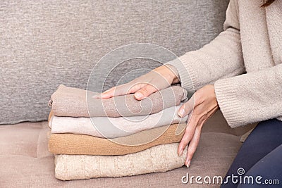 Female hands stack cozy knitted sweaters on the sofa. Warm concept Stock Photo