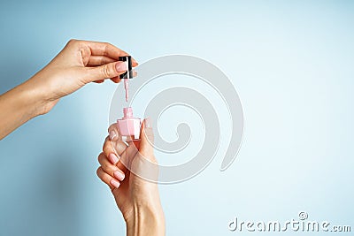 Spa and Manicure concept. Female hands with stylish french manicure, holds a bottle with nail polish on a blue background. With Stock Photo