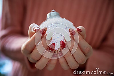 Female hands with stylish holiday manicure holding shiny white christmas bauble Stock Photo