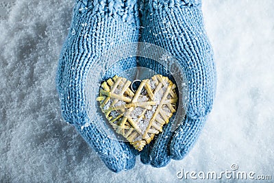 Female hands in teal knitted mittens with a entwined vintage romantic heart on a snow background. Love and St. Valentine concept Stock Photo