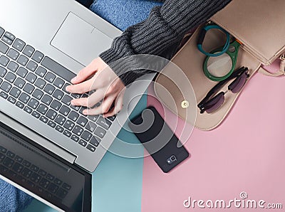 Female hands use a laptop on the background of a bag, smartphone, smart bracelet and other gadgets and accessories. Top view Stock Photo