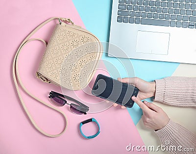 6Female hands use a smartphone on the background of a bag, laptop, smart bracelet and other gadgets and accessories. Top view Stock Photo