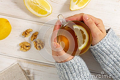 Female hands in warm sweater holding cup of tea with lemon on white wooden table Stock Photo