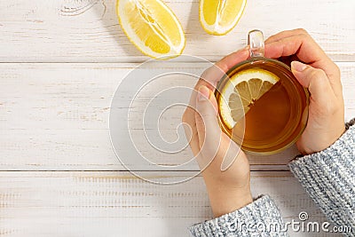 Female hands in warm sweater holding cup of tea with lemon on white wooden table Stock Photo