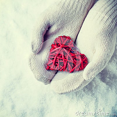 Female hands in white knitted mittens with a entwined vintage romantic red heart on a snow. Love and St. Valentine concept. Stock Photo