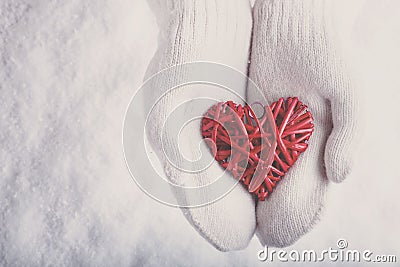 Female hands in white knitted mittens with a entwined vintage romantic red heart on a snow. Love and St. Valentine concept. Stock Photo