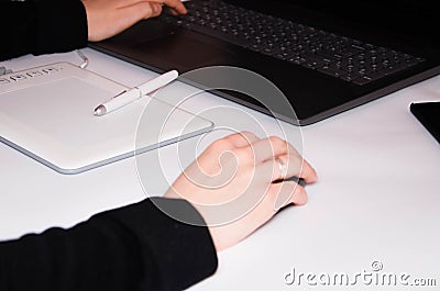 Female hands work on a graphic tablet. Hand holds stylus pen and draws. White graphic tablet. The work of a graphic designer. Girl Stock Photo