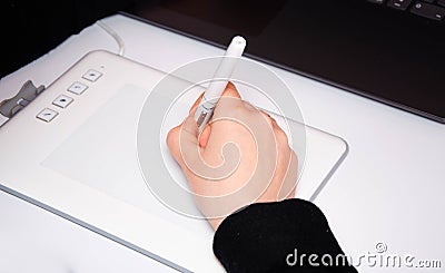 Female hands work on a graphic tablet. Hand holds stylus pen and draws. White graphic tablet. The work of a graphic designer. Girl Stock Photo