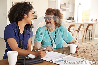 Female healthcare worker sitting at table smiling with a senior woman during a home health visit Stock Photo