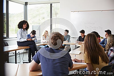 Female High School Tutor Sitting At Table With Pupils Teaching Maths Class Stock Photo