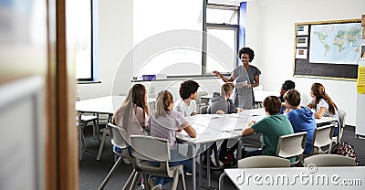 Female High School Tutor Standing By Table With Students Teaching Lesson Stock Photo