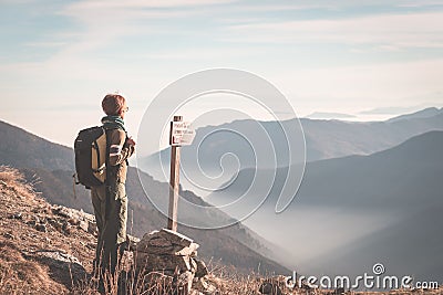 Female hiker with backpack looking at the majestic view on the italian Alps. Mist and fog in the valley below, snowcapped mountain Stock Photo