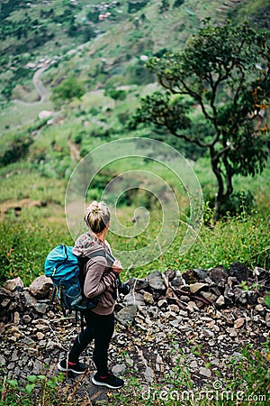 Female hiker with backpack walking down cobbled path to the lush green Paul valley. Santo Antao Cape Verde. Cabo Verde Stock Photo