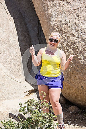 Female hiker gives a thumbs up after climbing up a giant boulder Stock Photo