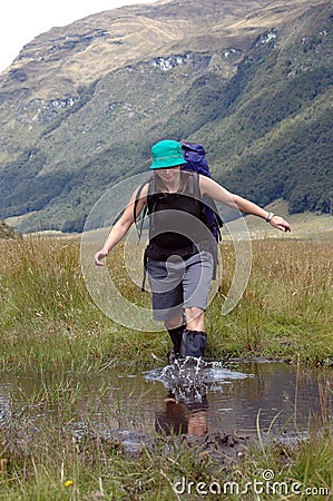 Female hiker wading thru a creek while tramping in New Zealand Stock Photo