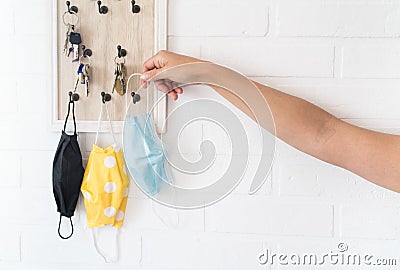 Female hinging the protective face mask on the keys organizer hook on the loft design white background brick wall in the home Stock Photo