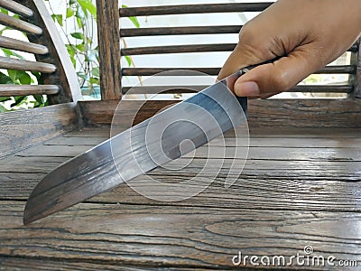 Female right hand with Steel kitchen knife on brown wooden chair Stock Photo