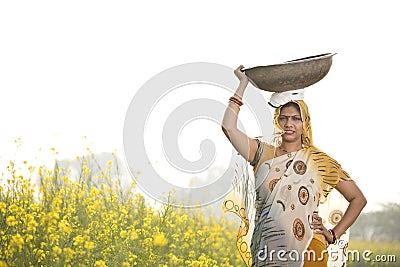 Female Indian farmer carrying iron pan on head in agriculture field Stock Photo