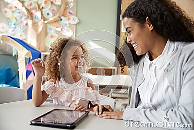 Female infant school teacher working one on one in a classroom using a tablet computer with a young mixed race schoolgirl, smiling Stock Photo