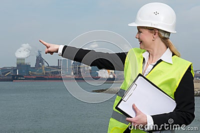 Female inspector in hardhat and safety vest pointing at industrial site Stock Photo