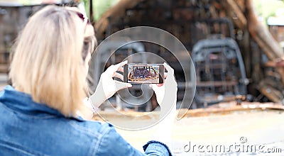 Female insurance broker or journalist photographs burned-out car after terrorist attack Stock Photo