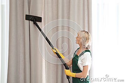 Female janitor removing dust from curtain Stock Photo