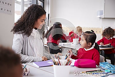 Female kindergarten teacher sitting at table in a classroom talking to a young Chinese schoolgirl, close up Stock Photo