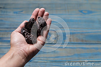 Female left hand holding prune on blue pinus wood Stock Photo