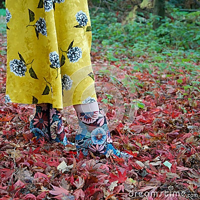 Female leg / foot walking in autumn leaves: floral ankle boot and yellow flares Stock Photo