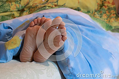 female legs under the blanket on the bed in the bedroom while sleeping, feet on the bed, the girl sleeps on the bed at Stock Photo