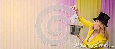 Female magician shows tricks takes a rabbit out of a hat. Woman magician in a yellow suit and hat shows miracles of magic Stock Photo
